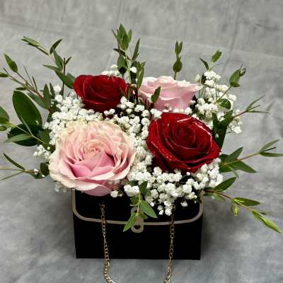 Pink and red roses arranged in a black box with white filler flowers
