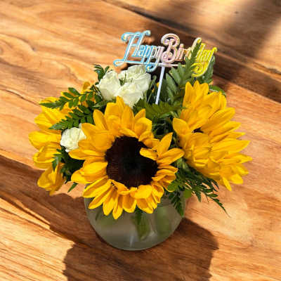 Sunflower and white rose arrangement in a glass vase with a Happy Birthday topper