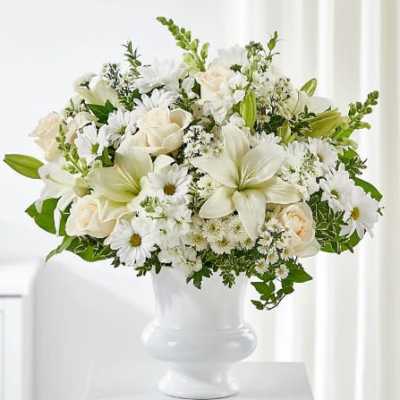 White floral arrangement in a white vase with roses, lilies, and daisies