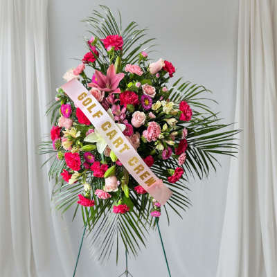 Standing floral wreath with pink flowers and a gold-lettered ribbon