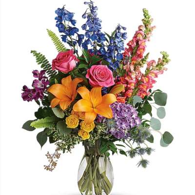 Tall mixed bouquet with orange lilies, pink roses, blue delphinium and purple hydrangea in a clear glass vase