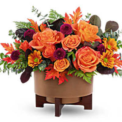 Orange roses and autumn flowers in a round vase on a wooden stand