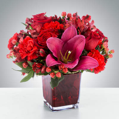 Red floral arrangement in a square glass vase with a large pink lily