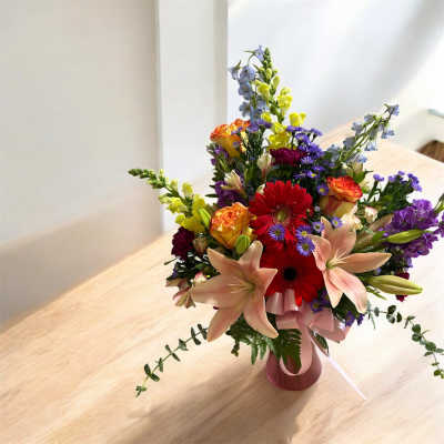 Bright mixed bouquet with lilies, roses, gerbera daisies and delphinium in a pink vase on a wooden table