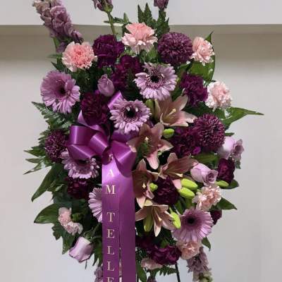 Standing purple and pink floral wreath on an easel with a ribbon