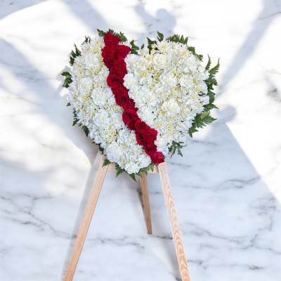 Heart-shaped white floral wreath with a red rose stripe on a wooden stand