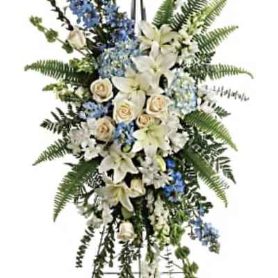 Standing funeral spray with white lilies, cream roses, and blue flowers on an easel