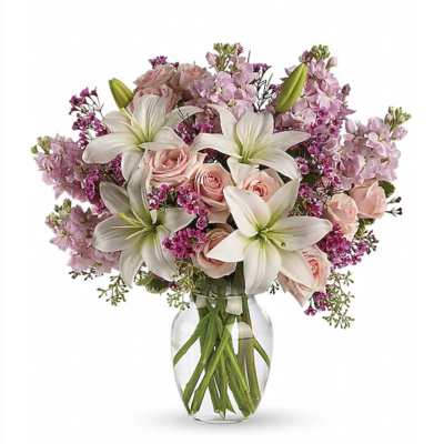Bouquet of white lilies and light pink roses with purple accents in a clear glass vase