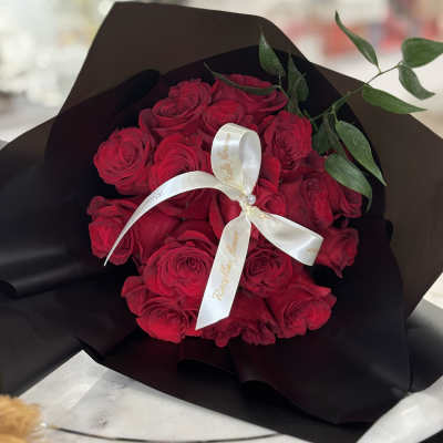 Bouquet of red roses wrapped in black paper with a white ribbon