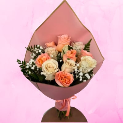 Hand-tied bouquet of peach and cream roses with baby's breath in pink wrapping paper