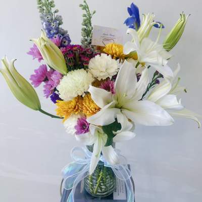 Mixed bouquet with white lilies, chrysanthemums, and purple flowers in a glass vase