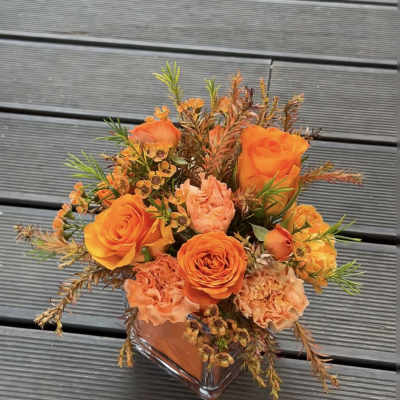Orange roses and peach carnations in a clear square vase