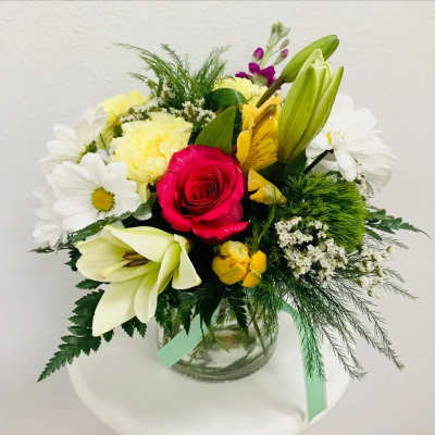 Mixed bouquet with a red rose, white lilies, and daisies in a glass vase