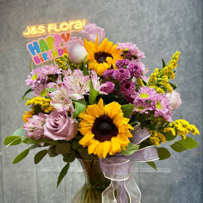 Mixed bouquet with sunflowers, pink roses, and purple blooms in a glass vase