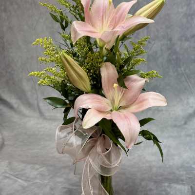 Pink lilies in a glass vase with a ribbon bow