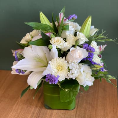 White floral arrangement in a green square vase with purple accents