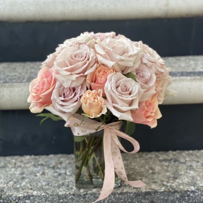 Bouquet of pale pink and peach roses in a clear glass vase with a ribbon