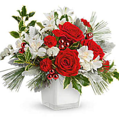 Red roses and white lilies in a white vase with holiday greenery