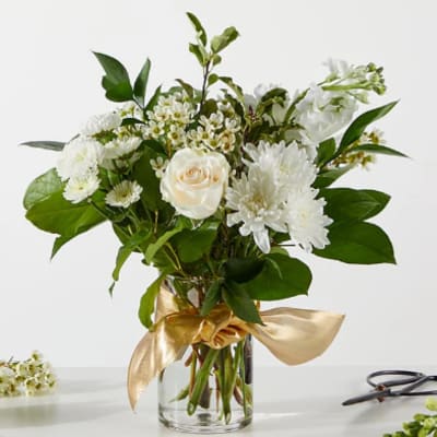White and cream flowers in a clear glass vase with a gold ribbon bow
