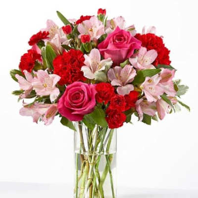 Pink roses, red carnations, and light pink alstroemeria in a clear glass vase