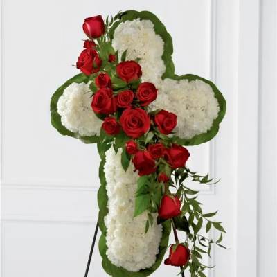 Cross-shaped floral tribute with red roses and white flowers on an easel