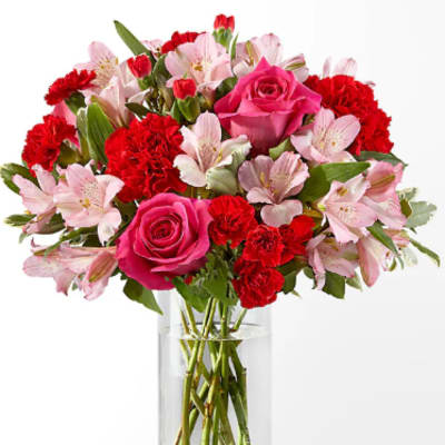 Arrangement of hot pink roses, red carnations, and pale pink blooms in a clear glass vase