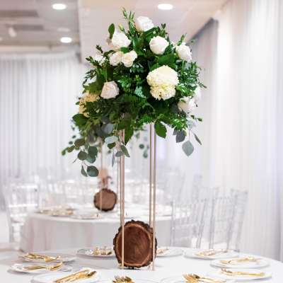 White floral centerpiece on a tall gold stand at a decorated table