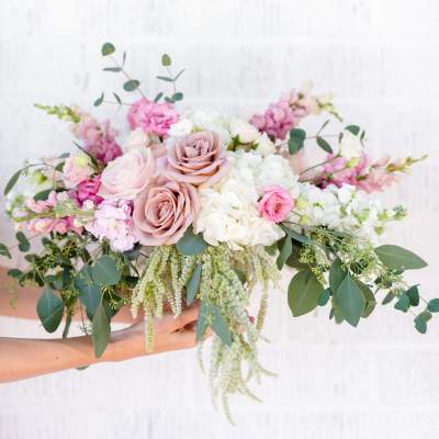 Handheld bouquet of blush and white flowers with trailing greenery