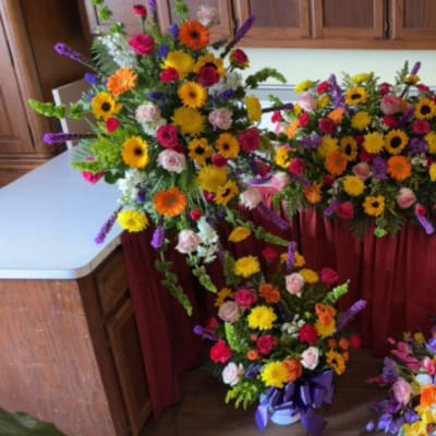 Set of bright mixed funeral sprays and a casket spray with yellow, pink, orange, and purple flowers.