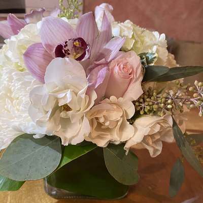 Pastel bouquet with orchids, roses, and white blooms in a glass vase