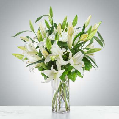 Tall arrangement of white lilies with buds in a clear glass vase