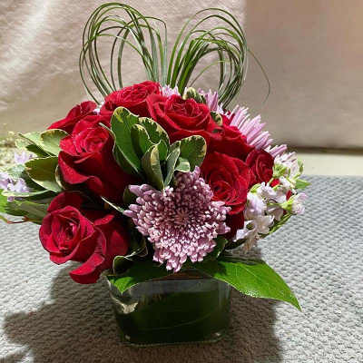 Red roses and lavender flowers in a square glass vase