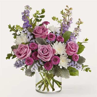 Pink roses and purple-white mixed flowers in a clear glass vase