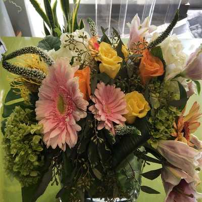 Mixed bouquet with pink gerberas, yellow and peach roses, and lilies in a glass vase