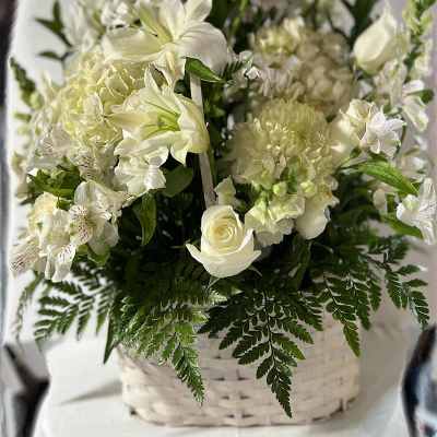 White floral arrangement in a white basket with lilies and roses