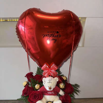 Red heart balloon above roses, a teddy bear, and chocolates in a white box