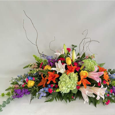 Low, elongated arrangement of colorful lilies, roses, hydrangeas, and mixed flowers.