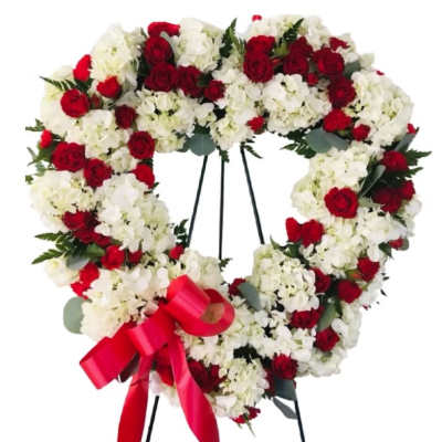 Heart-shaped wreath of red roses and white flowers on a stand with a red ribbon