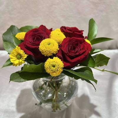 Red roses and yellow pom flowers in a clear glass vase