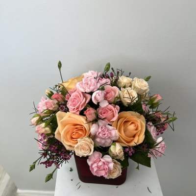 Pink and peach roses arranged in a burgundy box