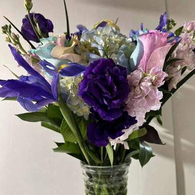 Mixed bouquet of purple, pink, and blue flowers in a clear glass vase