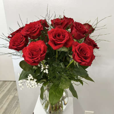 Tall arrangement of red roses with white filler flowers in a clear glass vase