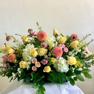 Large pastel floral arrangement with roses, dahlias, and hydrangeas in a low container