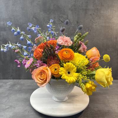 Mixed bouquet of orange, yellow, pink, and blue flowers in a white vase