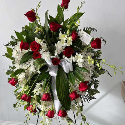 Standing floral wreath with red roses, white flowers, and a white ribbon on an easel