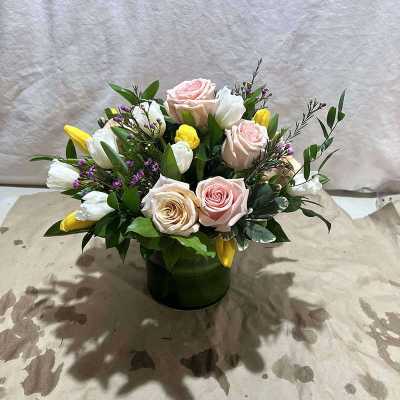 Mixed bouquet of pink roses, white tulips, and yellow blooms in a green vase