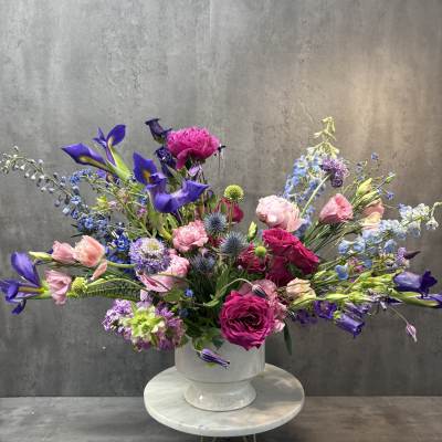 Large mixed bouquet of pink, purple, and blue flowers in a white pedestal vase