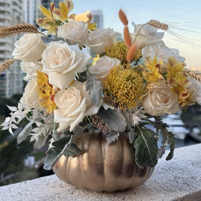 White roses and yellow flowers in a gold pumpkin vase