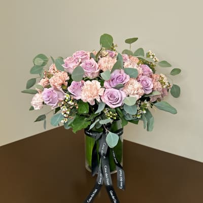 Pink roses and carnations arranged in a glass vase with a ribbon