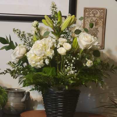White roses and lilies arranged in a black basket vase